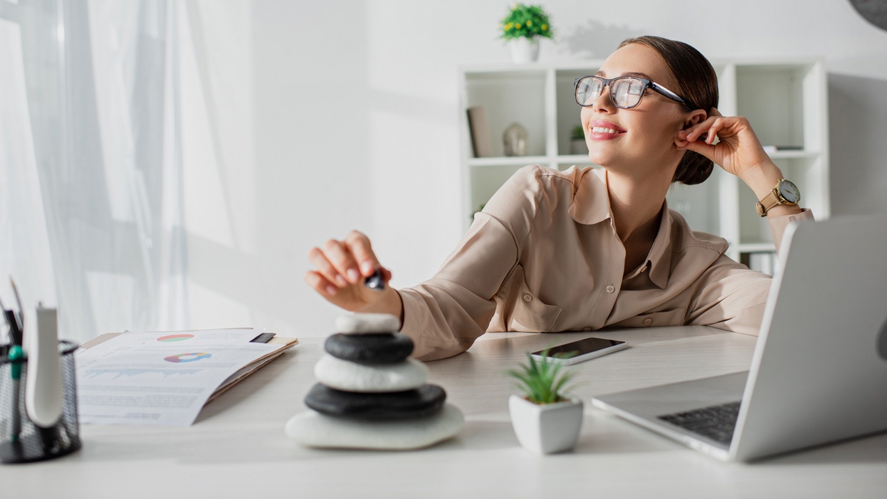 dreamy businesswoman sitting at workplace with zen stones and laptop