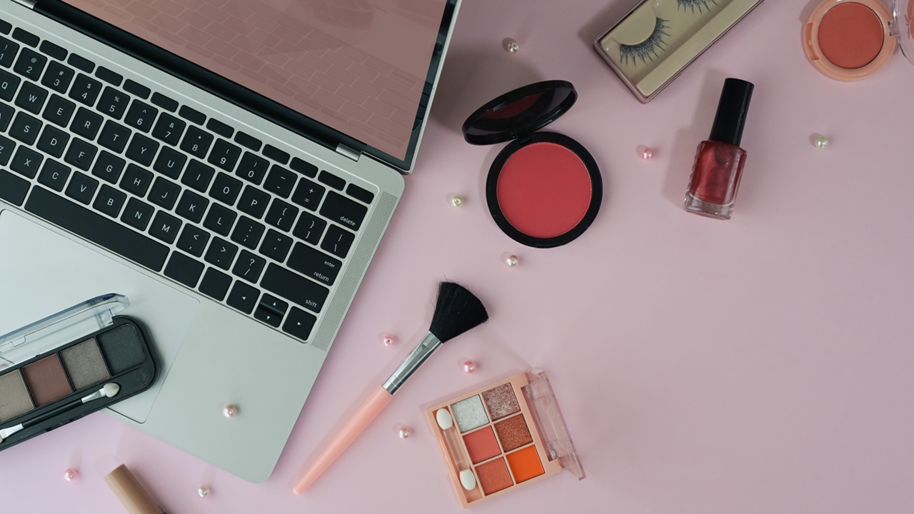 Top view feminine workspace with laptop and cosmetics on pink ba