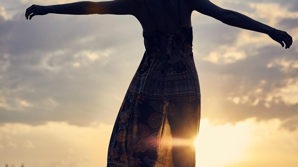 Woman with open arms facing a golden sunset, a hopeful image for the flexible future of mental healthcare, by Josh Trent Wellness and Wisdom
