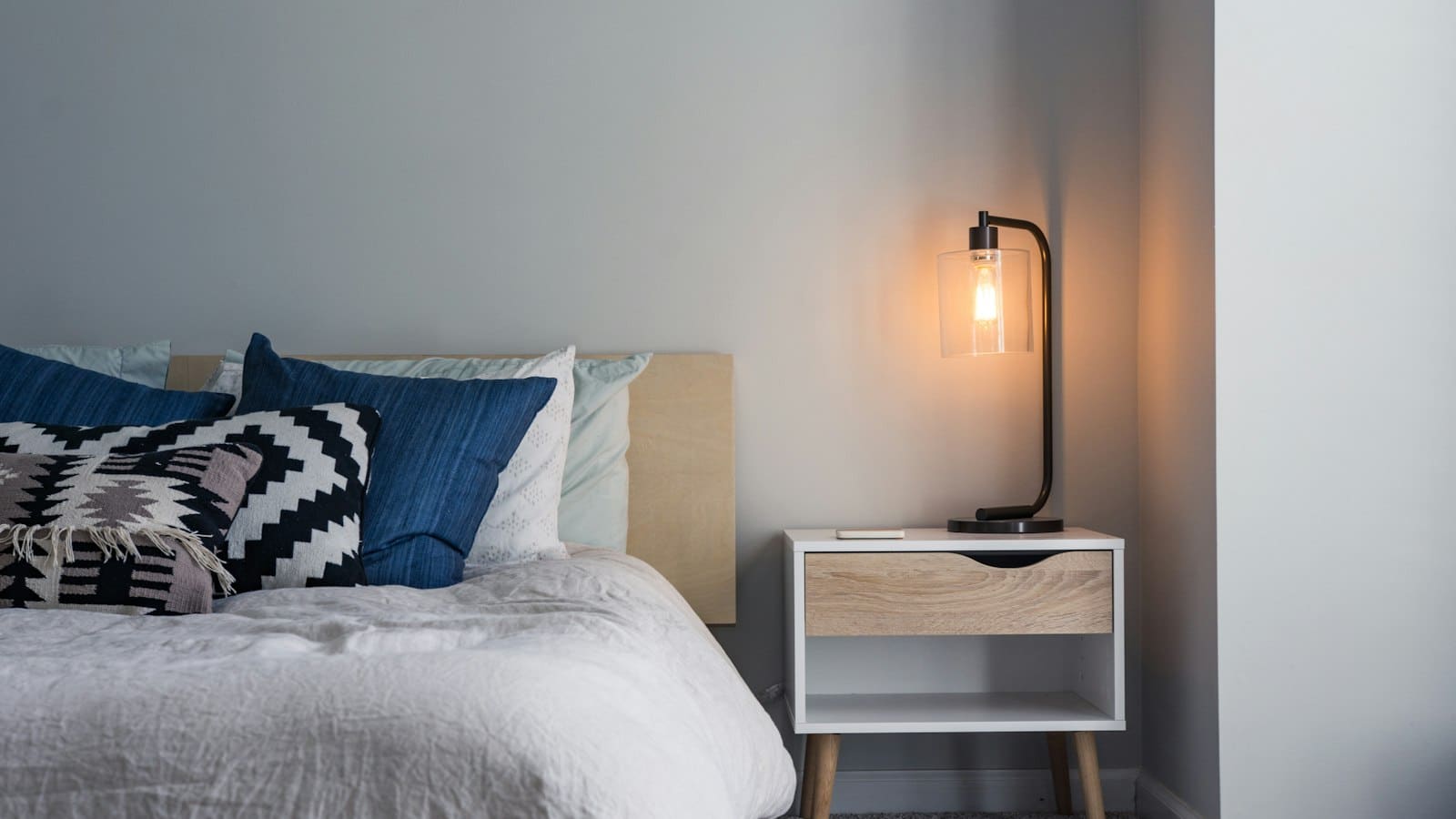 Peaceful bedroom with soft pillows and a warm bedside lamp, a restful image for how to sleep better by Josh Trent Wellness and Wisdom