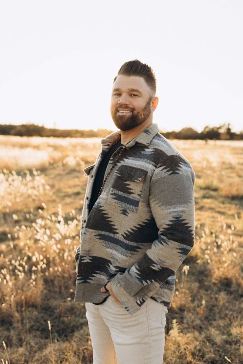 Man smiling outdoors with natural landscape, embracing wellness, mindfulness, and holistic wisdom for healthy living.